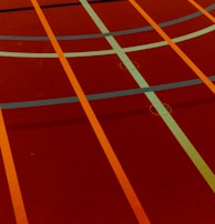 A sports court with intersecting lines in orange and blue, creating geometric patterns on a reddish-brown surface.